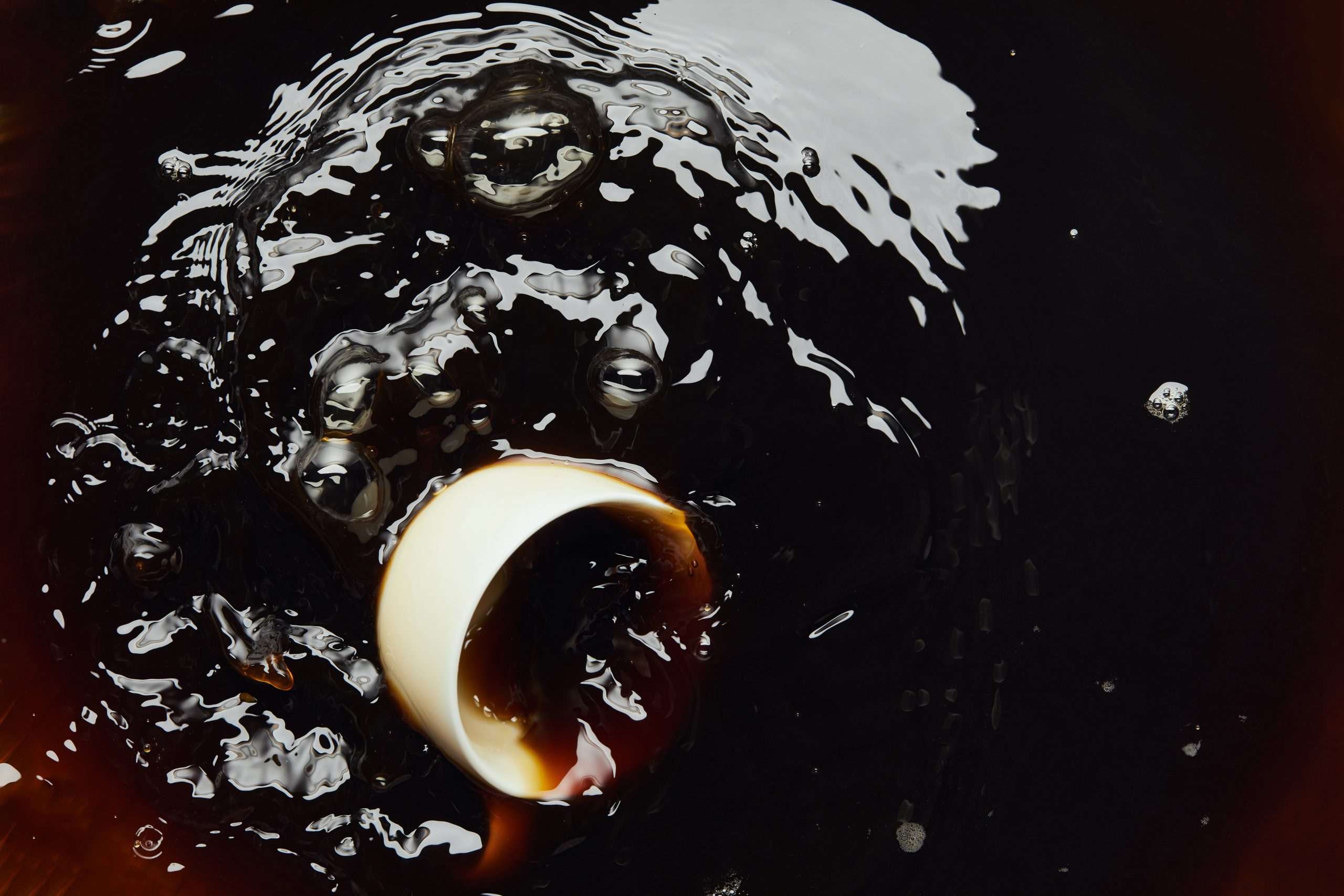Overturned porcelain white cup and black coffee with bubbles