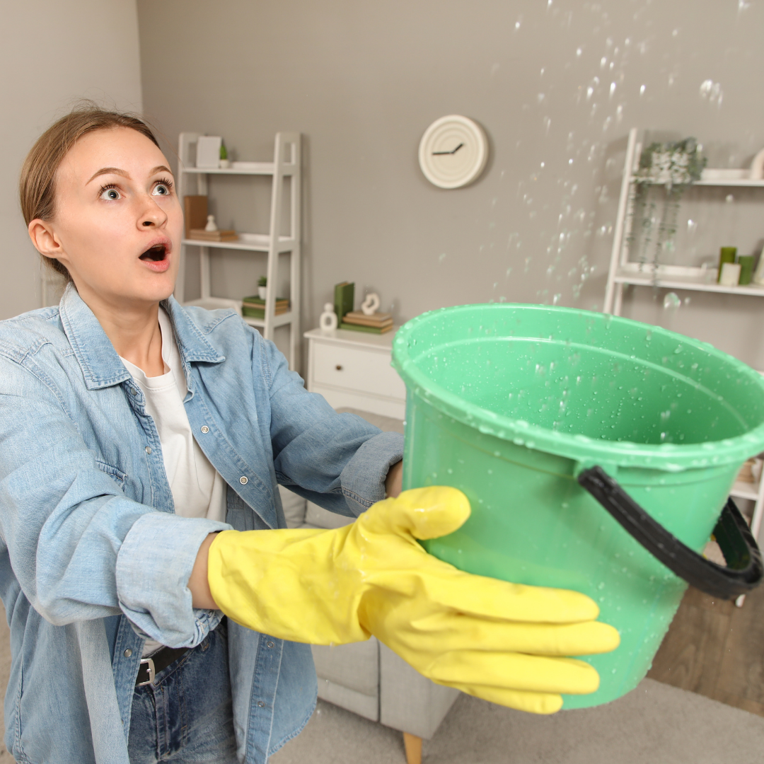 homeowner catching water from ceiling leak with bucket during emergency plumbing situation inside house